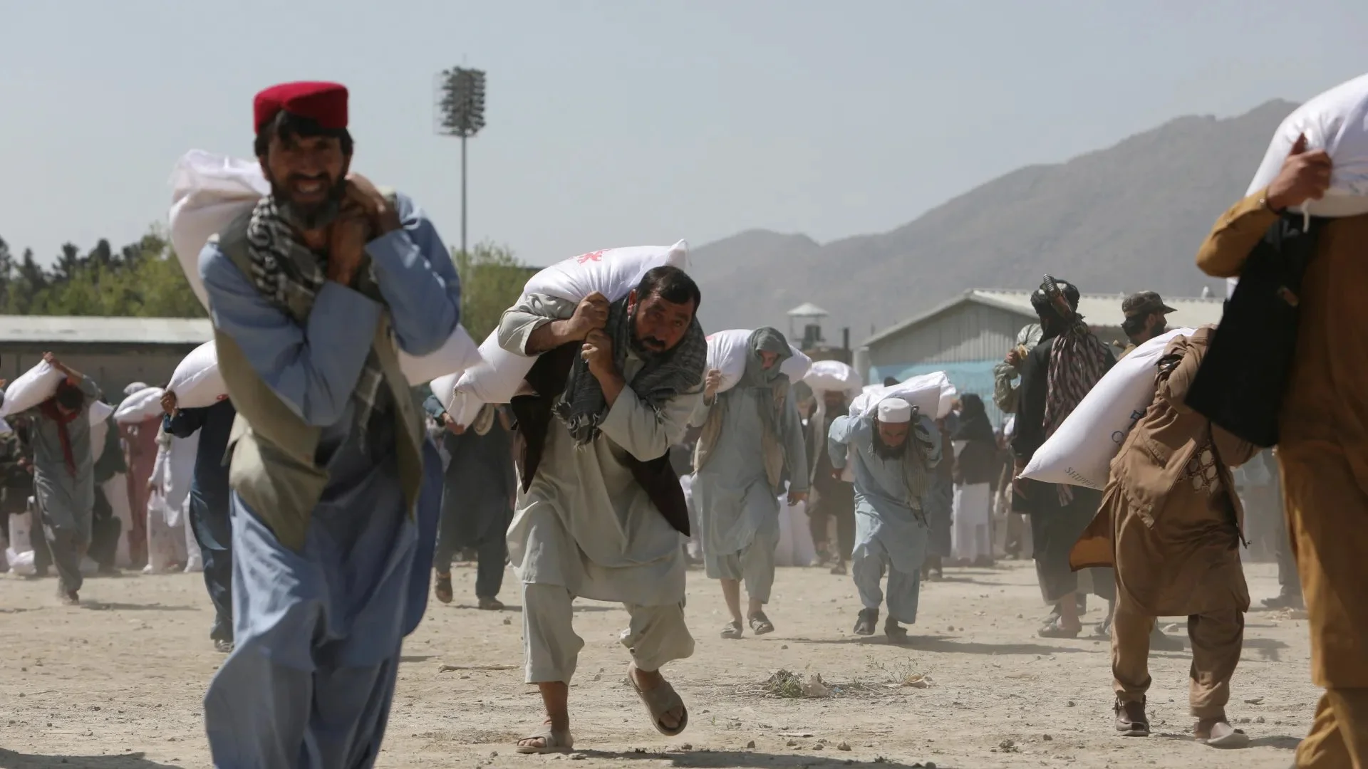 Afghan people carry sacks of rice, given out as part of humanitarian aid sent by China to Afghanistan, at a distribution centre in Kabul, Afghanistan on April 7, 2022 [Reuters]