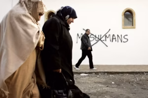 Muslim residents walk past racial slurs painted on the walls of a mosque in the town of Saint-Étienne in central France. © Laurent Cipriani/AP