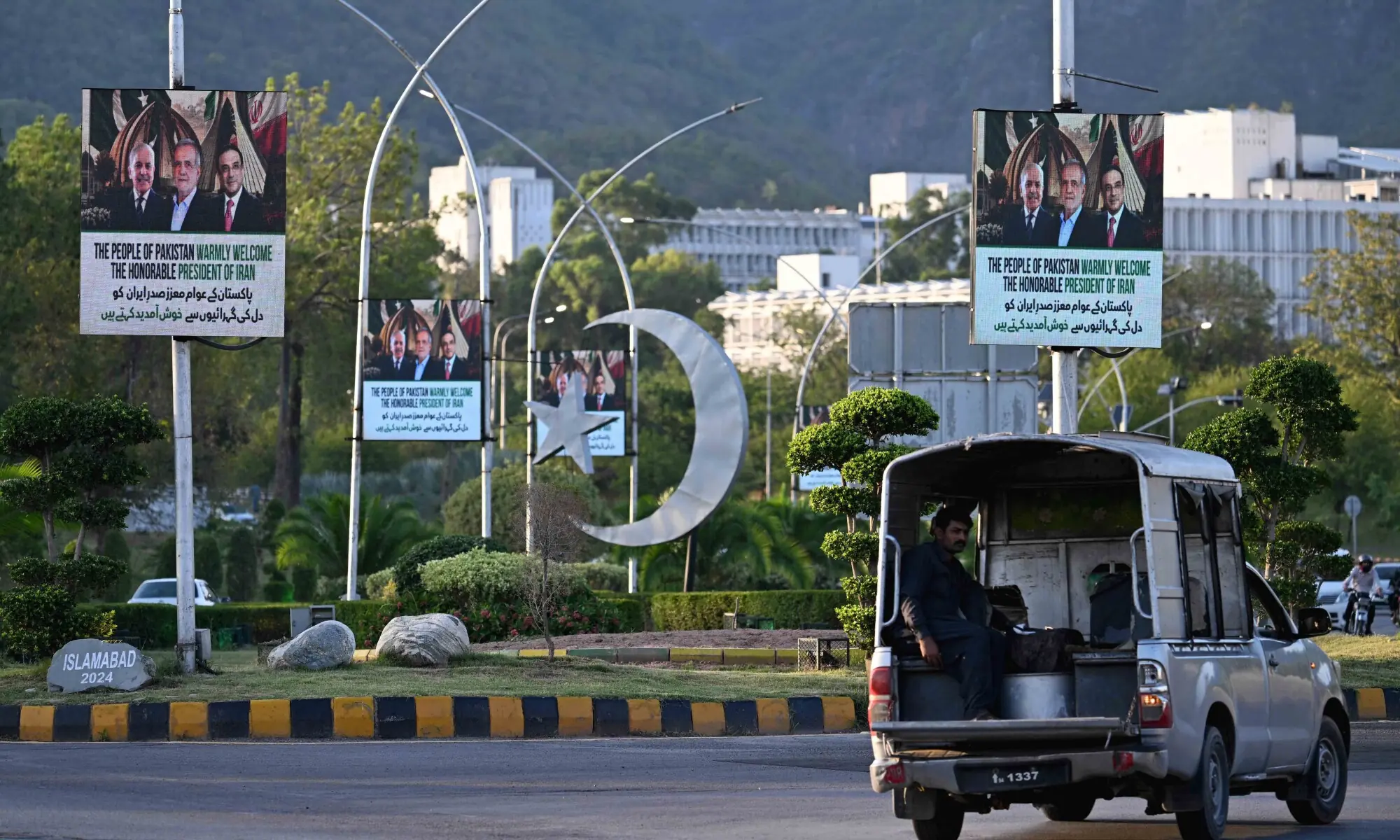 A commuter rides past electronic boards featuring Iran's President Masoud Pezeshkian (C), Prime Minister Shehbaz Sharif (L) and President Asif Ali Zardari, displayed along a street in Islamabad on June 22, 2026. — AFP