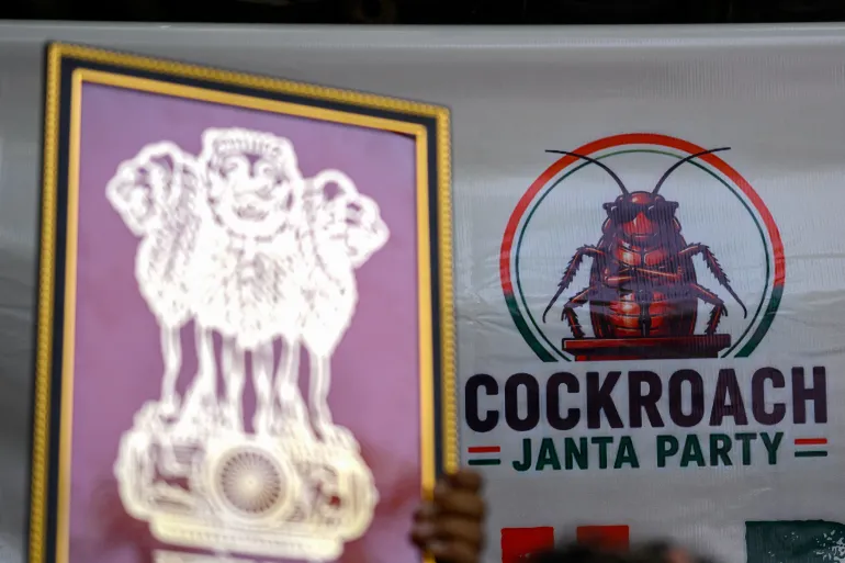 The Cockroach Janta Party (CJP) logo is pictured in the background as a supporter holds India's national emblem during a protest over alleged irregularities in the country's major examinations, in New Delhi. - AFP